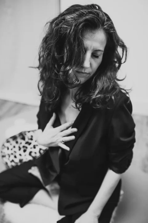 Jasmin in schwarzem Blazer. Sie hat die Augen geschlossen und die Hand auf dem Herzen.