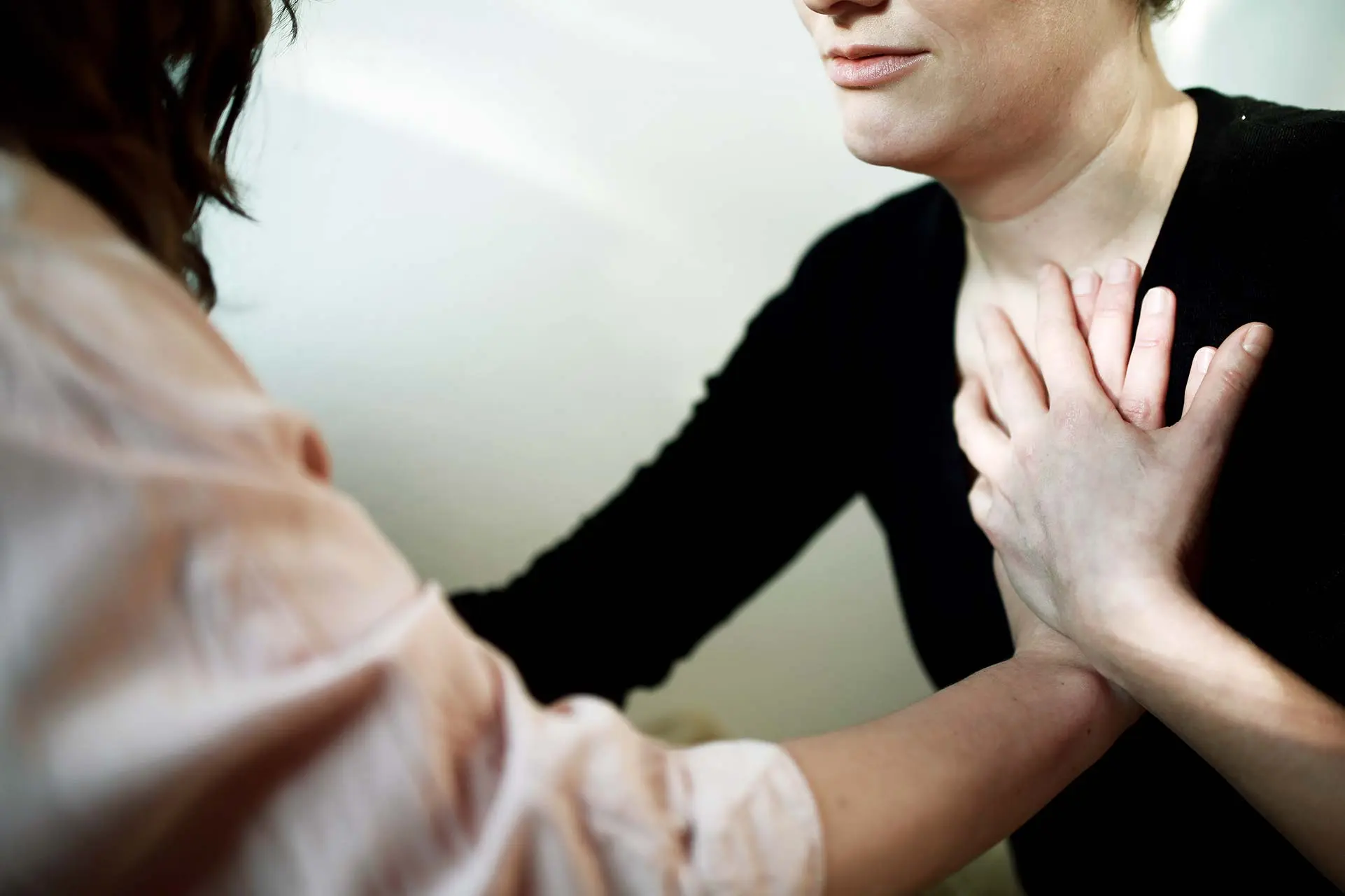 Zwei Frauen sitzen sich Gegenüber mit der Hand auf dem Herzen der jeweils Anderen.