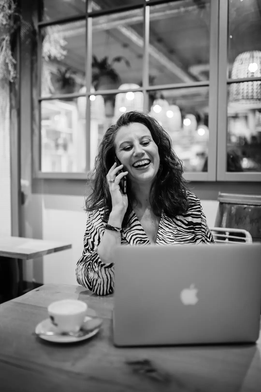 Jasmin telefoniert lachend vor dem Laptop in einem Cafe.