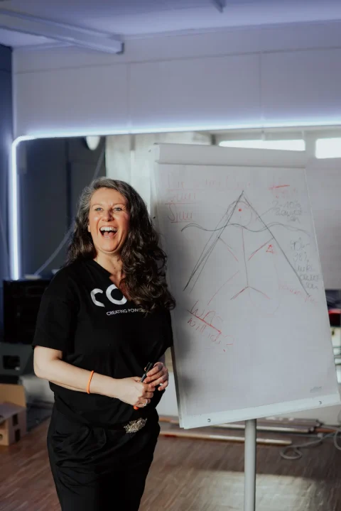 Jasmin steht laut lachend neben einem Flipchart.